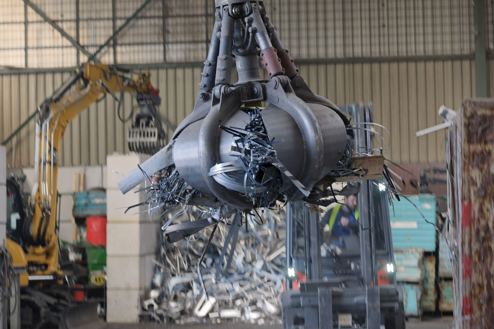Clamshell grapple lifting scrap metal inside a commercial warehouse